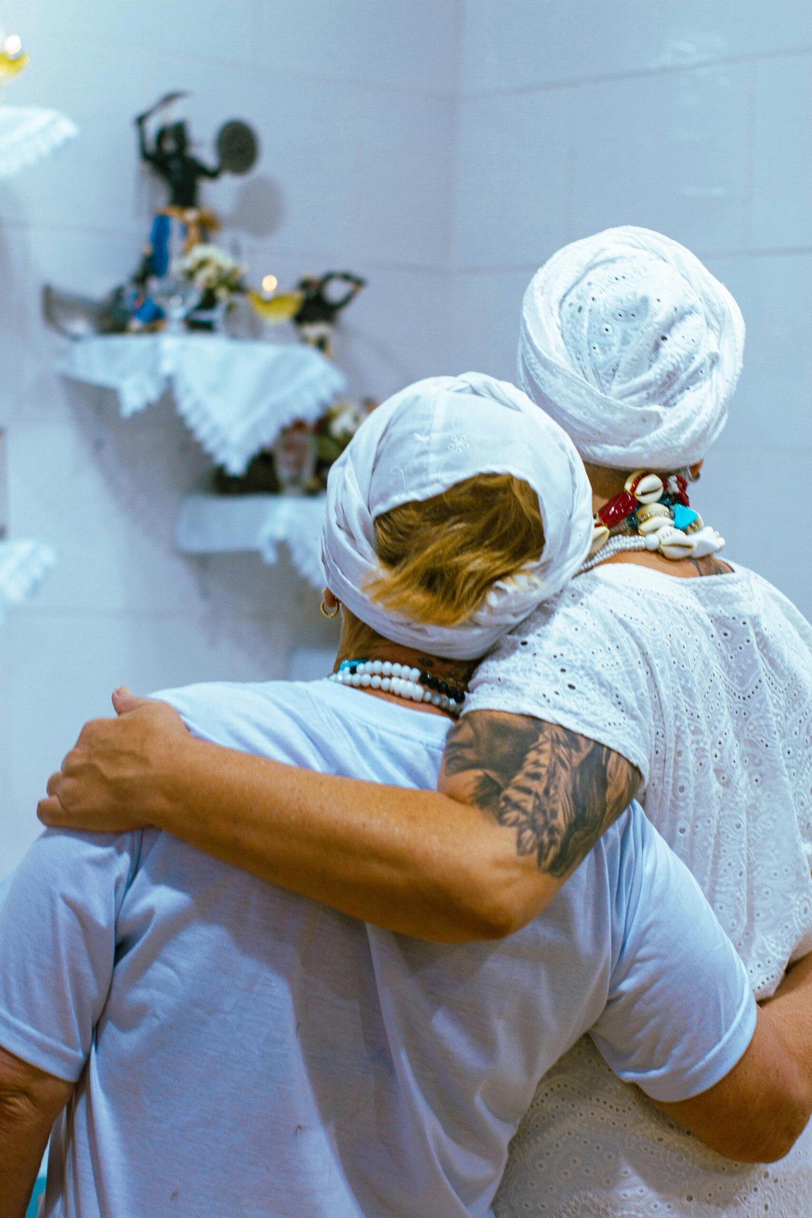 Two people in white embrace in a spiritual room, sharing warmth and connection.