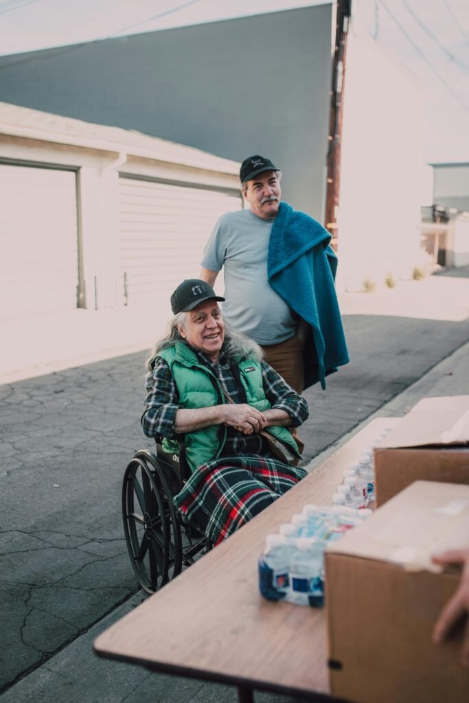 A heartwarming moment as volunteers distribute essentials to an elderly man in a wheelchair outdoors.