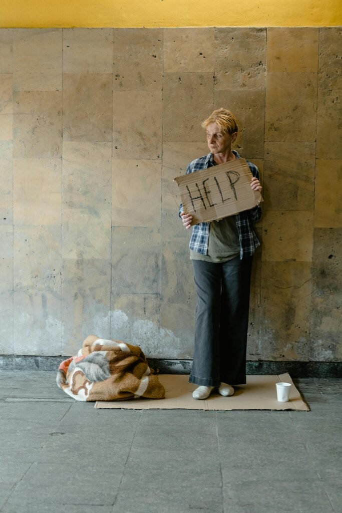 An elderly woman stands holding a cardboard sign that reads 'HELP,' conveying a sense of homelessness and need.